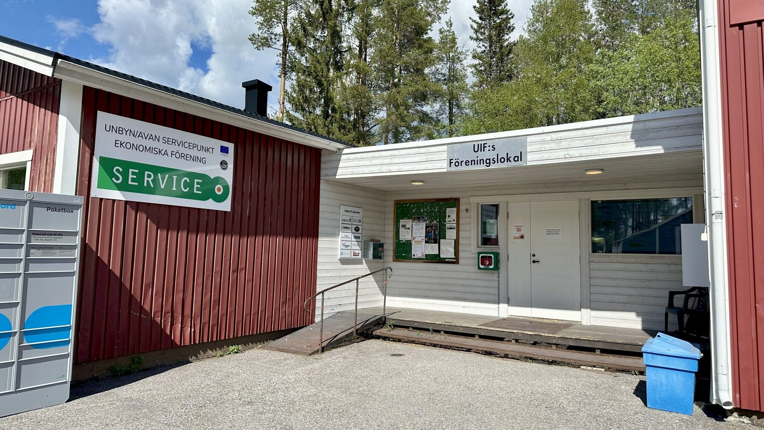 Unbyn En röd träbyggnad med en skylt med texten UNEK UNBY/UNAN SERVICENHET EKONOMISKA FÖRENING SERVICE och en annan för UIF:s Föreningslokal. Utanför entrén finns anslagstavla, ramp och blå soptunna.